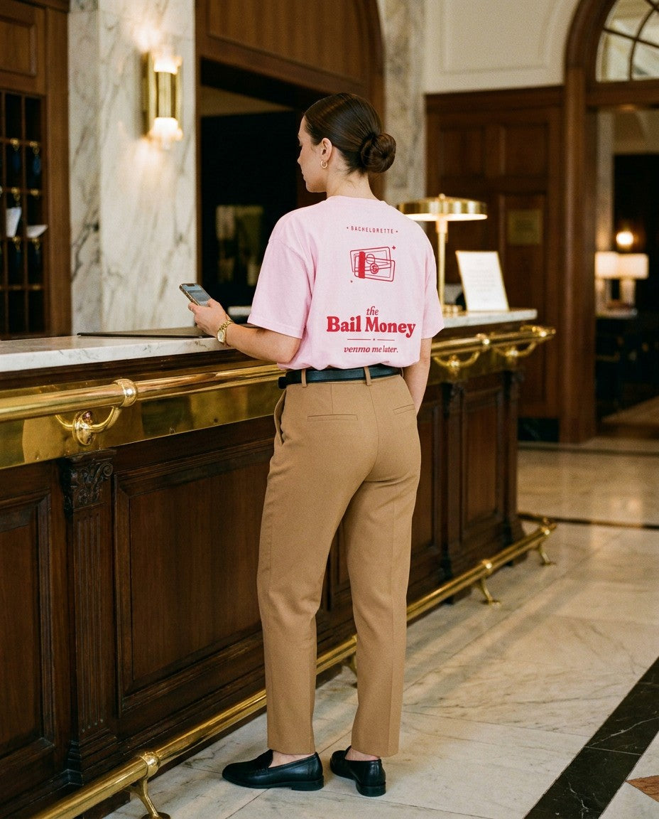 The Bail Money Oversized Tee in Blossom with camel trousers at a hotel desk