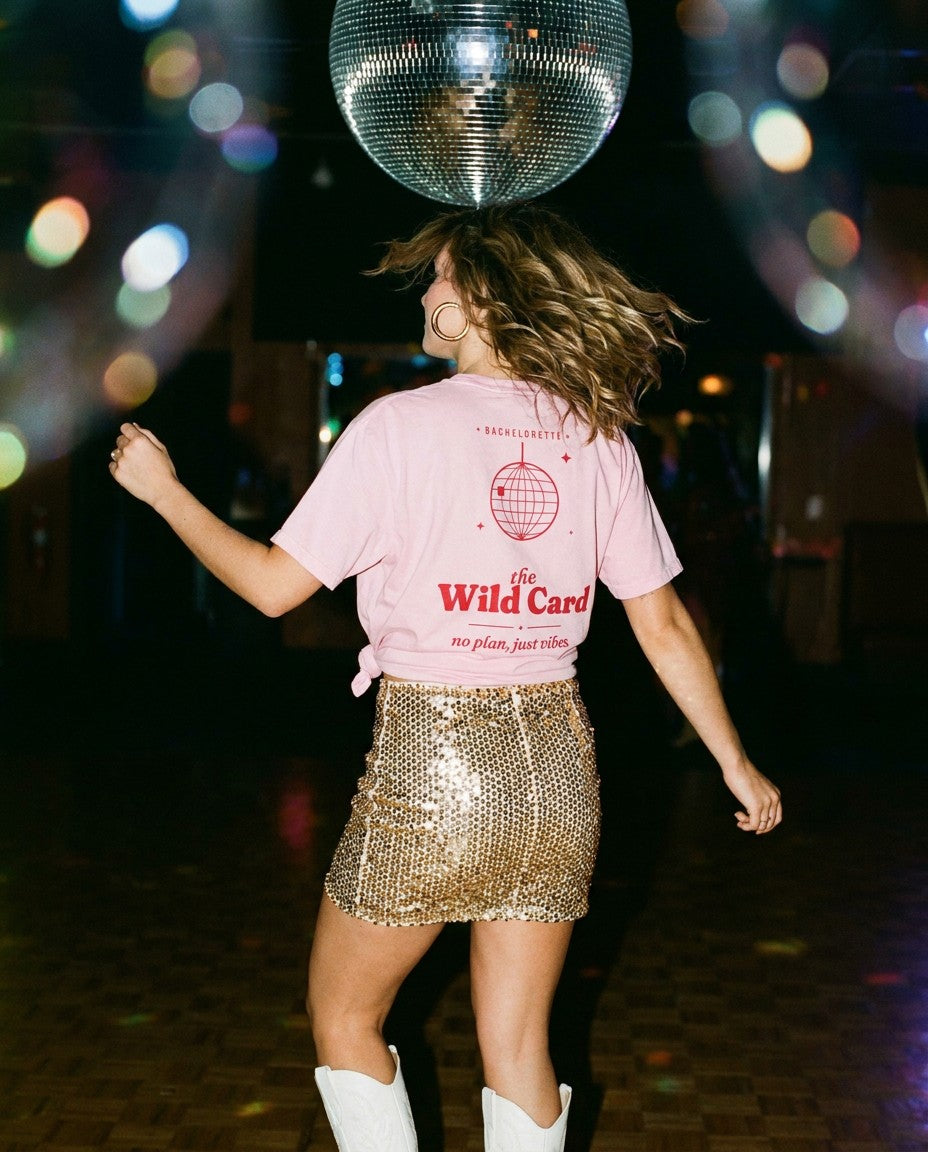 The Wild Card Oversized Tee in Blossom knotted over a gold sequin skirt under a disco ball